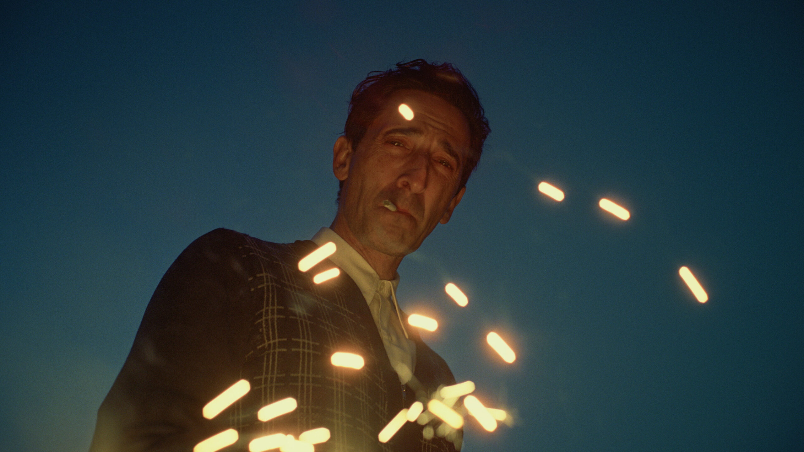 Adrien Brody as 'László Tóth' in 'The Brutalist' staring at the camera with industrial sparks