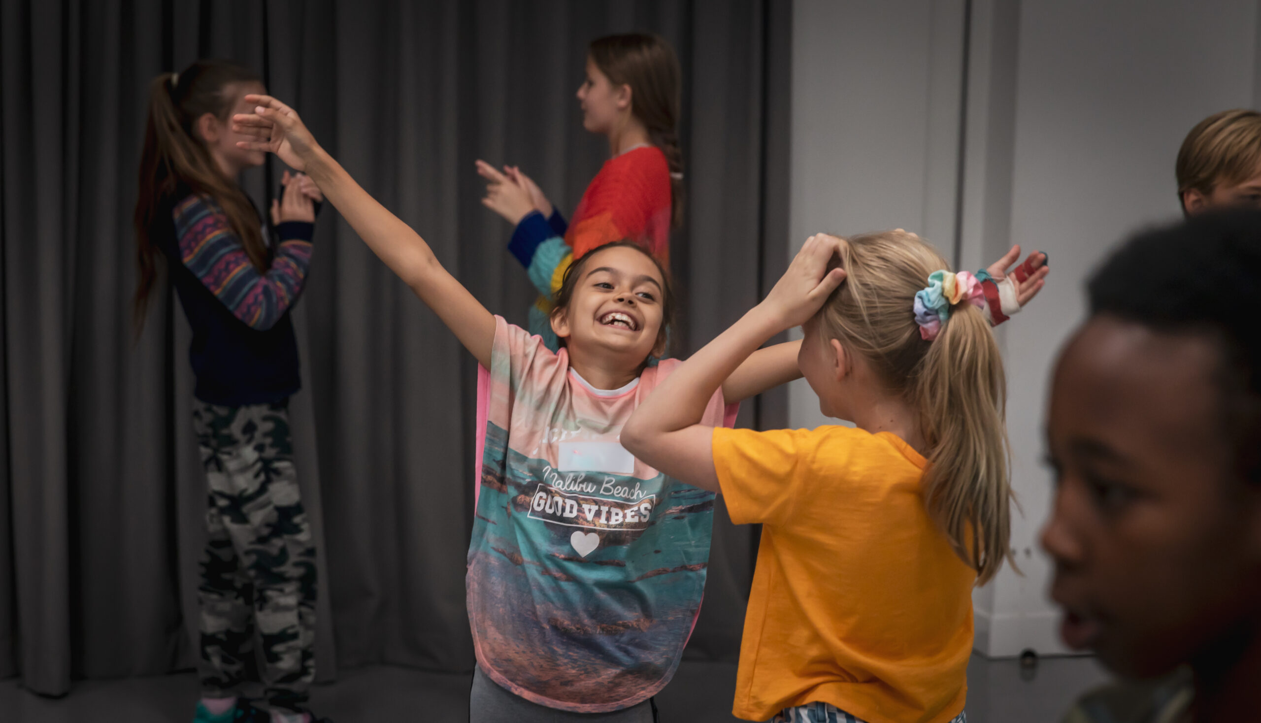 A young actor looking happy with her arms in the air while she participates in a workshop with other young actors