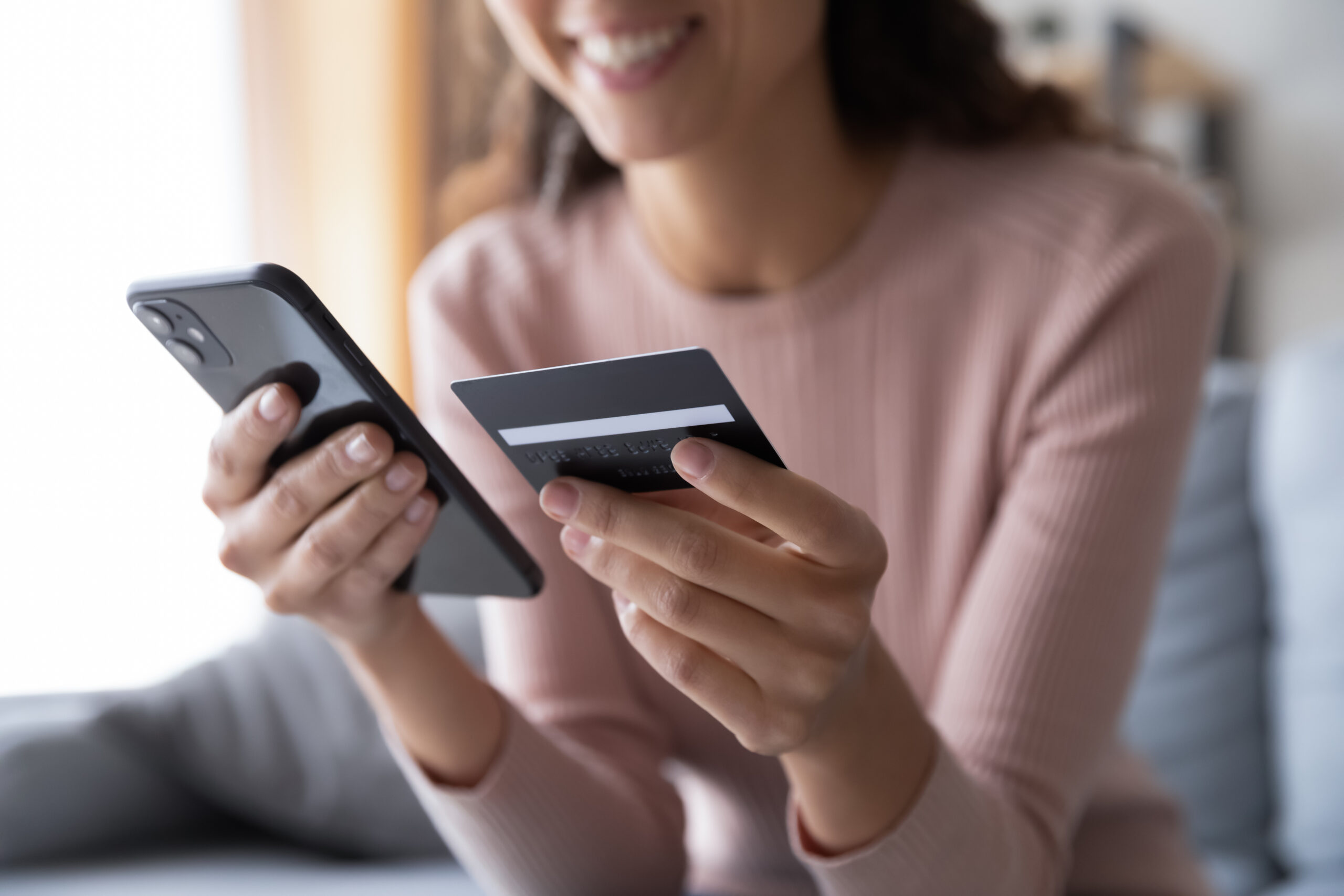 A woman holding her credit card and her phone while she shops online