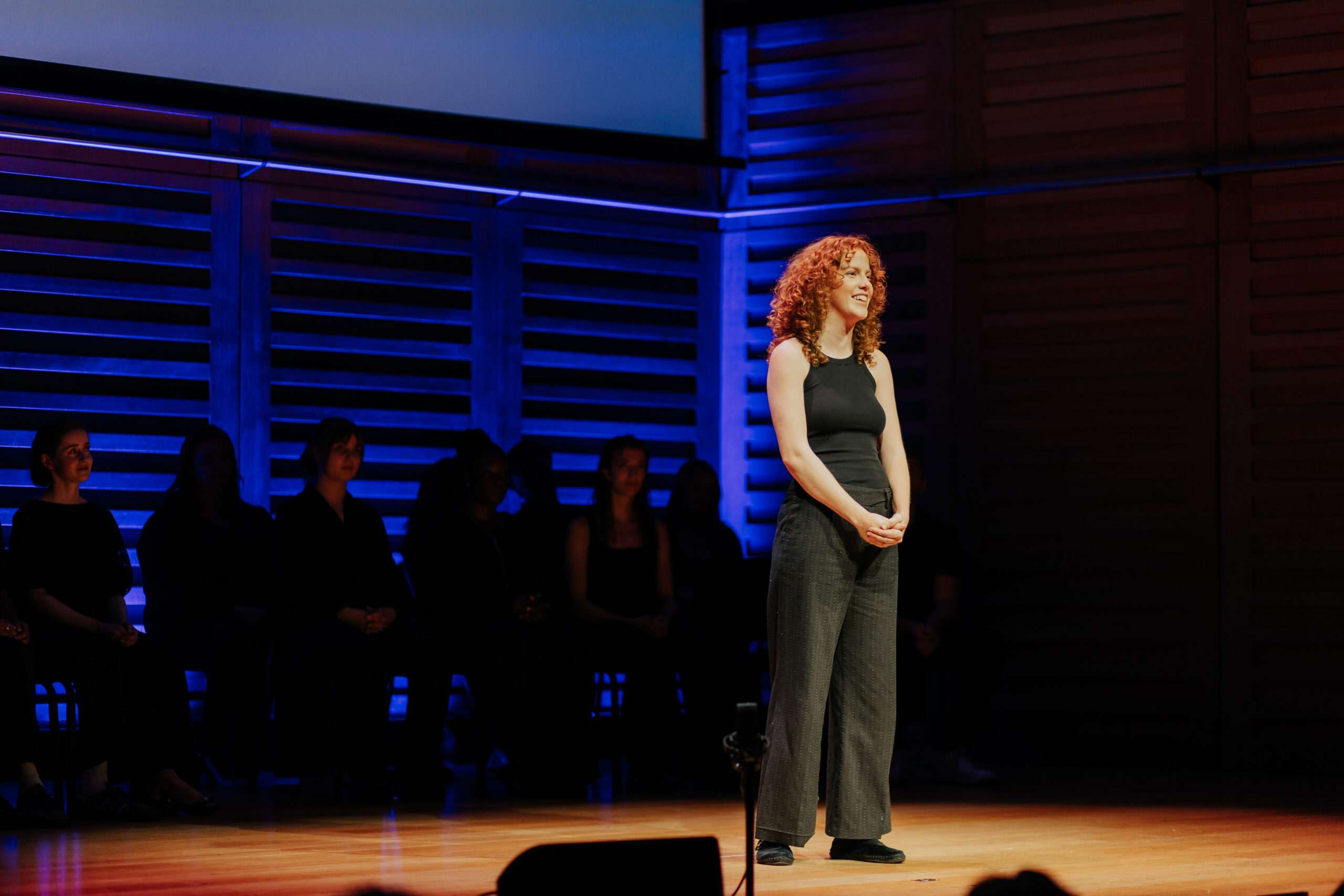 A red-haired actress smiling as she performs on stage during the Spotlight Prize showcase.